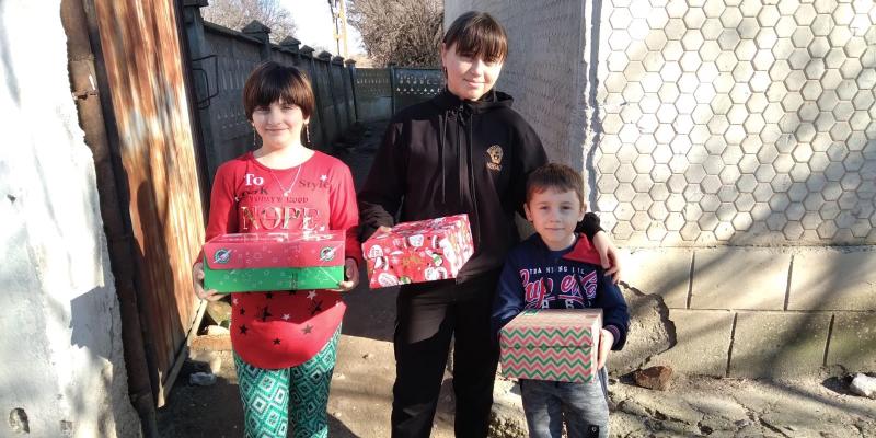 Three children outside with shoebox gifts