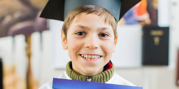 Boy in graduation hat holding The Greatest Journey Certificate
