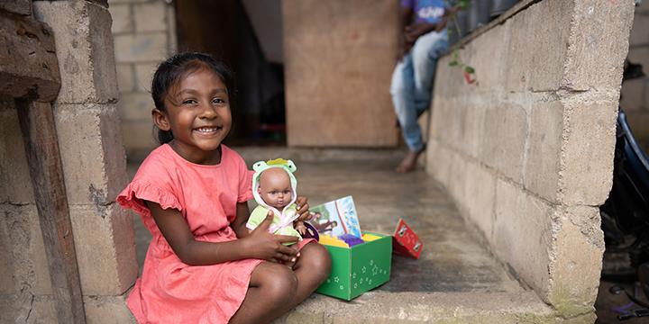 girl in pink dress with shoebox gift and doll