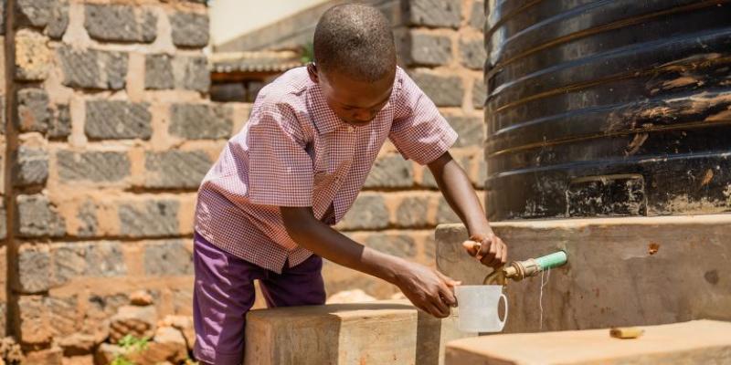 A STUDENT IN KENYA TESTS THE WATER SYSTEM, PREPARING TO ENJOY A DRINK OF CLEAN WATER.