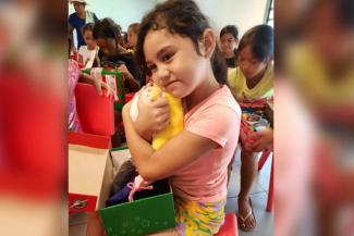 A girl in French Polynesia hugs the stuffed “wow” toy that was packed in her shoebox gift.