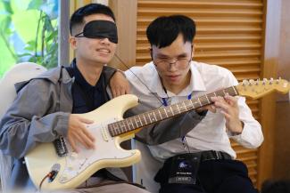 Minh helps an attendee at “Dining in the Dark” learn how to play the guitar while blindfolded.